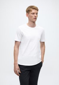 T-shirt bianca a maniche corte con scollo rotondo, tessuto liscio e orlo curvo, abbinata a pantaloni scuri a gamba affusolata.