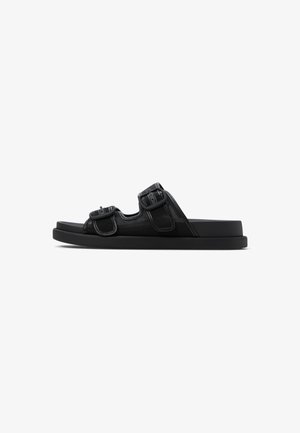 Sandales noires à glissière avec deux sangles réglables à boucle, une tige texturée et une semelle plate en caoutchouc, présentant un design minimaliste.