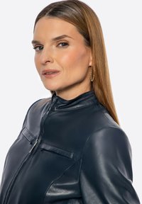 Dunkelblaue Lederjacke mit hohem Kragen, ausgestattet mit zwei Brusttaschen und einer glatten Textur. Das Modell zeigt die Jacke von der Seite.