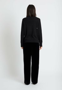 Pull en maille noir avec un col rond, associé à un pantalon large en velours noir. Présente un petit logo dans le dos du pull.