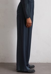 Marineblauwe wijde broeken van gladde stof met een elastische tailleband, voorzien van zijzakken en een relaxte pasvorm. Draag ze met zwarte platte schoenen.