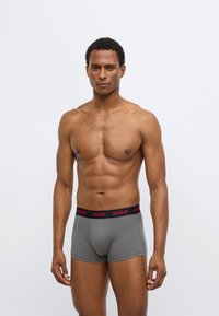 Gray cotton boxer briefs with a black waistband featuring red “HUGO” branding, offering a snug fit and minimalistic design.