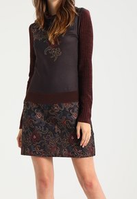 Pull noir avec des manches marines côtelées et des motifs floraux brodés sur la jupe ; possède un col montant et une silhouette ajustée.