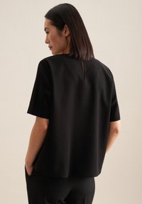 Top nero a maniche corte con scollo rotondo e piccolo dettaglio cut-out sulla schiena, realizzato in un tessuto morbido con vestibilità ampia e design minimal.