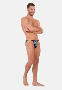 Blumiger Herren-String-Tangas mit schwarzem Hintergrund und lebhaften pinken und grünen Mustern, aus glattem, dehnbarem Stoff gefertigt.