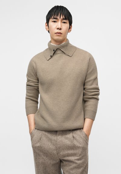 Μπεζ ριγωτό πουλόβερ με όρθιο γιακά και δύο κουμπιά, συνδυασμένο με καφέ υφασμάτινο παντελόνι με υφή. Διαθέτει εφαρμοστή γραμμή και πλεκτή υφή.