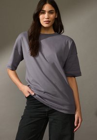 Grauer kurzärmeliger Sweatshirt mit lässiger Passform und rundem Ausschnitt, kombiniert mit schwarzen Jeans. Glatte Stoffoberfläche und aufgerollte Ärmelschäfte.