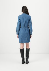 Denimkjole med lange ermer, belte i midjen og bakstykke. Kombinert med svarte skinnstøvler til knærne. Glatt tekstur, lyseblå farge.