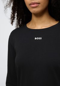 Mustast pehmest kangast pika varrukaga t-särk, millel on rinnal valge "BOSS" logo ja klassikalise ümar kaelusega.