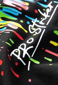 Färgglad tyg med en svart bas och ljusa, abstrakta stänk i grön, blå, röd och gul. Vit text meddelar "ProStriker."