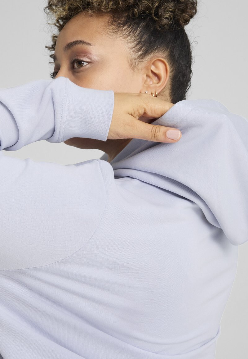 Jasnoniebieska bluza z kapturem o miękkiej fakturze, z luźnym krojem i sznurkiem na kapturze. Widoczne przeszycia i subtelne detale na rękawach.