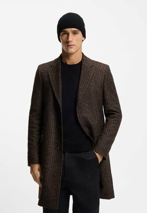 Ruskea houndstooth-takki, jossa on rakenteellinen muotoilu, kontrastivärinen musta neule alla ja sovitettu musta neulottu pipo. Sileä pinta, räätälöity istuvuus.