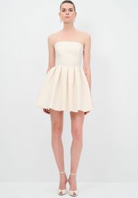Robe crème sans bretelles avec un corsage ajusté et une jupe plissée évasée, fabriquée en tissu lisse. Présente un design épuré et un matériel minimal.