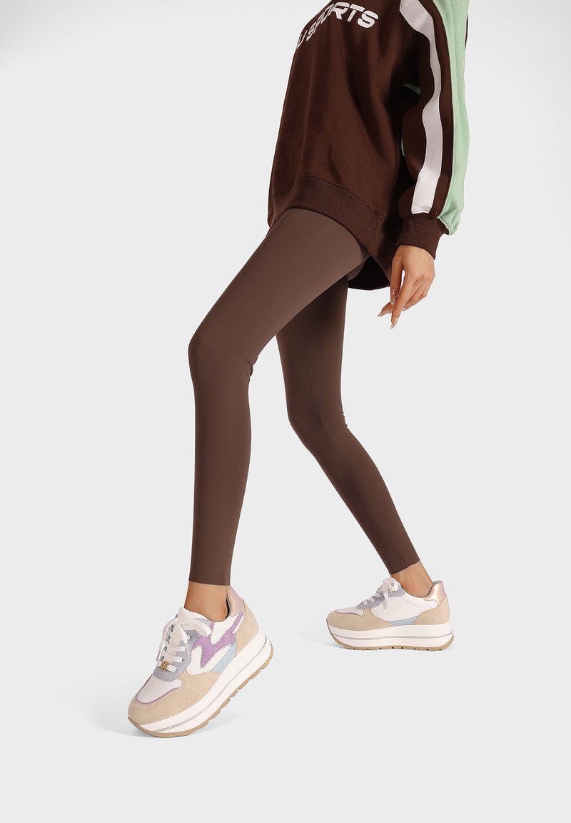 Leggings marron associés à un sweat-shirt surdimensionné marron avec des rayures vertes et blanches. Les chaussures comprennent des baskets beiges avec des accents violets.