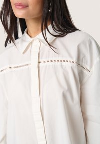 Witte katoenen shirt met een kraag, met een knoopsluiting en een horizontale uitsnijding over de borst. Glad textuur en een relaxte pasvorm.