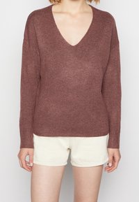 Mörkröd V-ringad tröja gjord av mjukt stickat tyg, med långa ärmar och ribbade muddar, tillsammans med krämfärgade shorts.