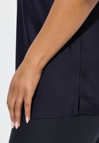 Marineblaue Sportoberteil mit glatter Textur, kurzen Ärmeln und seitlichen Schlitzen; kombiniert mit schwarzen Leggings, die einen lässigen Schnitt zeigen.