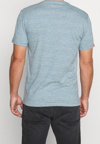 Camiseta de color azul claro jaspeada con mangas cortas, escote redondeado y un pequeño acento naranja en la manga derecha. Textura de tela suave.