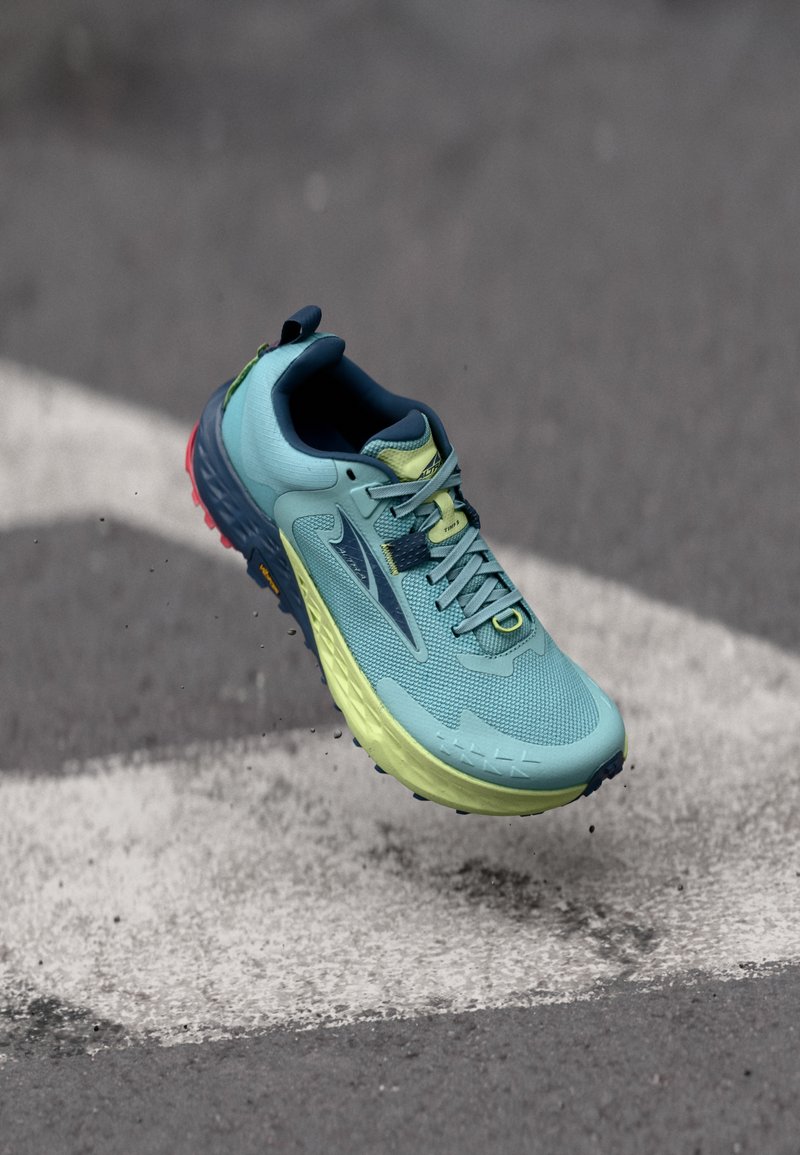 Running shoe in light blue mesh material with yellow accents, featuring a textured sole, and a raised heel. Visible lacing and logo detail.
