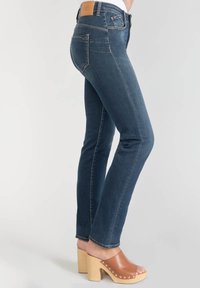 Mörkblå denimjeans med en anpassad design, raka ben och synlig sömnad. Kombineras med bruna träklackar.