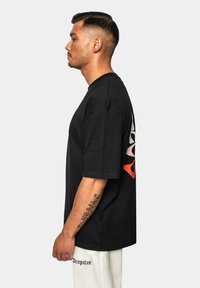 Sort kortærmet t-shirt med et livligt grafisk design i rød, pink og grøn på ryggen. Blødt bomuldsstof, afslappet pasform.