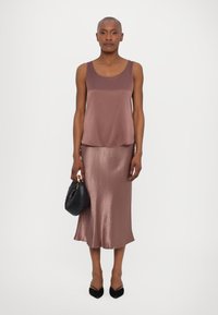 Satin tank top and mid-length skirt in mauve. Smooth texture, relaxed fit. Model holds a black quilted handbag, wearing pointed black heels.