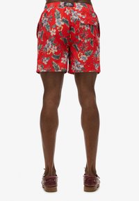 Los pantalones de baño florales rojos presentan un vibrante patrón de flores tropicales y hojas, con una cómoda cinturilla elástica y un bolsillo de parche.