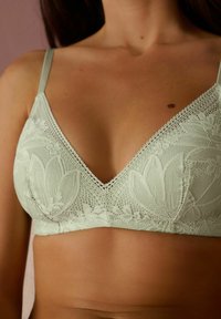 Ljusgrön spetsbralette med triangulär form, blommönster och detaljerad kant. Mjuk textur med justerbara band.