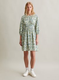 Robe florale en tissu léger, avec des motifs verts et bleus, manches longues, taille cintrée et jupe évasée, associée à des baskets blanches.