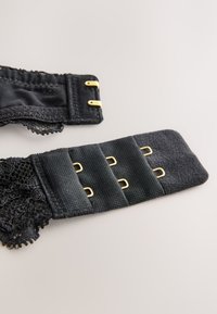 Allonge de soutien-gorge noire avec crochets dorés et trois rangées pour réglage de la taille sur un fond neutre.