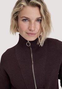 Dunkelbrauner, gerippter Pullover mit hohem Kragen und einem silbernen Reißverschluss-Detail. Verfügt über strukturierten Stoff und ein tailliertes Design.