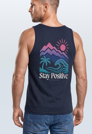 Mann trägt ein marineblaues Tanktop mit buntem Grafikdruck von Bergen, Sonne, Palme, Welle und dem Text „Stay Positive Nevertheless“ auf dem Rücken.