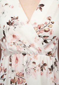Bloemen wikkel jurk van witte stof met roze en bruine bloemenpatronen, v-hals en een geregen taille voor een aansluitende silhouet.