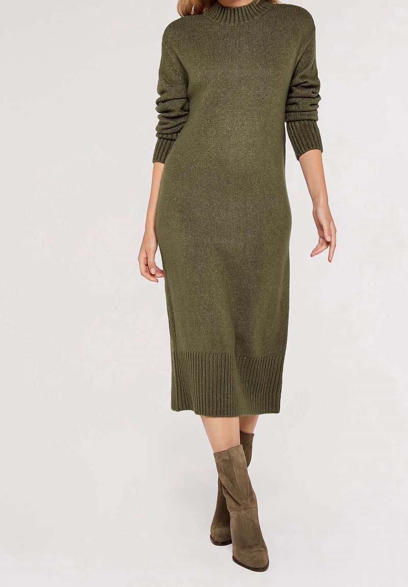 Femme portant une robe midi en maille côtelée vert olive à manches longues, associée à des bottes en daim marron mi-mollet.