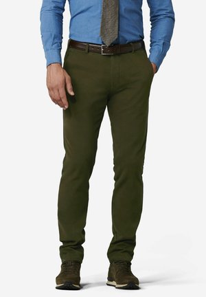 Mann trägt olivgrüne Hose, blaues langärmeliges Hemd, graue Krawatte, braunen Gürtel und braune Schuhe, steht mit einer Hand in der Tasche.