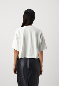 Hvit cropped t-skjorte med korte ermer og rund hals, kombinert med et svart lærskjørt med synlige sømmer og glidelås bak.