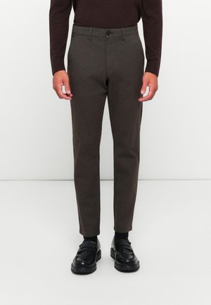 Brown wool trousers with a tapered shape, featuring a button closure and side pockets, paired with black loafers and dark socks.