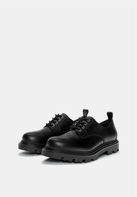 Pantofi din piele neagră cu vârf rotunjit, accente texturate și design cu șireturi. Include o talpă groasă, robustă pentru durabilitate.