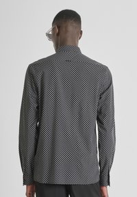 Camicia nera a stampa geometrica, con maniche lunghe e colletto a ribattino, realizzata in un tessuto liscio.