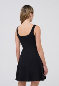 Abito nero senza maniche con corpetto aderente e gonna svasata. Tessuto liscio, scollo a barca e lunghezza sopra il ginocchio. Design semplice e pulito.