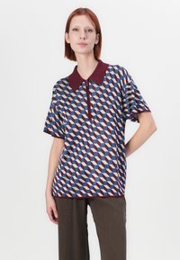 Polo majica kratkih rukava s geometrijskim uzorkom u tamnoplavoj, maroon i krem boji, s zatvaranjem na zip i kontrastnim ovratnikom.