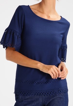 Top blu navy a maniche corte con accenti in pizzo ad occhio scallopato sulle maniche e sull'orlo. Tessuto liscio, scollatura rotonda, design aderente.