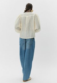 Kermalace pusero puffattuilla hihoilla, yhdistettynä vaaleansinisiin leveisiin farkkuihin, jotka korostavat rentoa istuvuutta ja tekstuurisia yksityiskohtia.