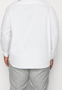 Vit långärmad skjorta med en mjuk textur, rundad nederkant och knäppte manschetter, matchad med grå rutiga byxor med ett rutmönster.