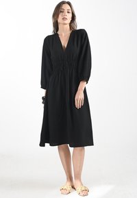 Abito nero con scollatura a V profonda, vita arricciata e maniche a sbuffo di tre quarti. Tessuto leggero con una silhouette A-line fluida.