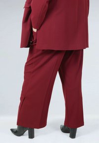 Burgundy suit featuring wide-leg trousers and a tailored blazer, made of smooth fabric with a subtle texture. Black block-heeled boots.