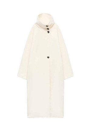 Cappotto lungo e oversize di colore crema, con colletto alto, chiusura frontale con bottoni e maniche corte. Realizzato in tessuto morbido e testurizzato. Design semplice.