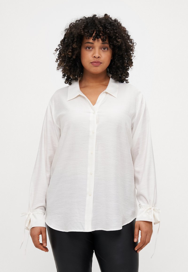 Camicia bianca a maniche lunghe con chiusura a bottoni, morbida al tatto e con dettagli a cravatta sui polsini. Presenta un colletto classico e una vestibilità rilassata.