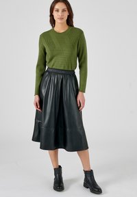 Pull en maille verte avec texture côtelée, associé à une jupe en cuir noir en forme A et des bottines noires. La tenue met en valeur un contraste de matériaux.