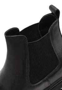 Botín negro de cuero con paneles laterales elásticos, punta redondeada, superficie texturizada y una silueta elegante. Notables acentos a rayas en negro.